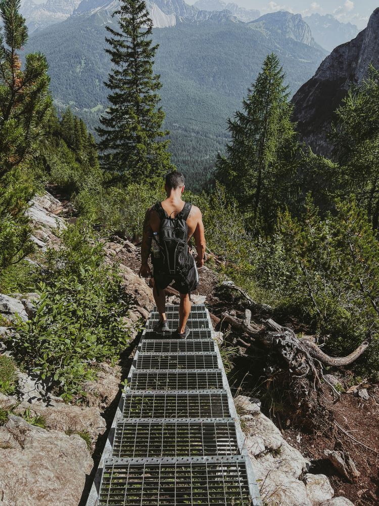 escaleras empinadas de hierro en la montaña y chico sin camiseta con mochila bajando por ellas lago sorapis